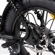 Close-up of a black fat tire bicycle wheel with a disc brake, rear suspension spring, and kickstand on a white studio background.