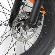 Close-up of a bicycle front wheel showing a silver disc brake rotor, black fork and tire, and an orange caliper accent on a white studio background.