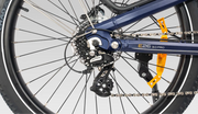 Close-up of a bicycle rear wheel showing the blue frame, disc brake rotor, chainring, cassette, derailleur, chain, and orange reflector on a light gray background.