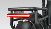 Close-up of a black bicycle rear rack with a horizontal red taillight illuminated, mounted above a black fender on a light gray studio background.