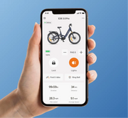 A hand holding a smartphone displaying a bike app interface with a blue electric bicycle shown on the screen against a solid blue background.