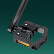 A close-up of a black bicycle pedal with a textured grip surface and a reflective yellow-orange strip on the underside, shown against a dark green gradient background.