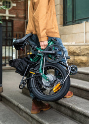 Person holding a folded green bicycle on outdoor steps.