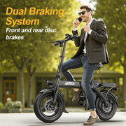A man in a brown blazer and jeans sits on a black KHRIDE folding electric bike, holding a phone to his ear. The image features promotional text on the top left reading 'Dual Braking System Front and rear disc brakes' against a blurred background of green trees and a building.